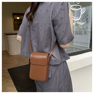 Primer plano de un bolso bandolera de cuero marrón vintage con un traje gris