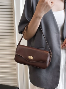 Minimalist dark brown leather shoulder bag with a gold oval twist lock for summer 2025
