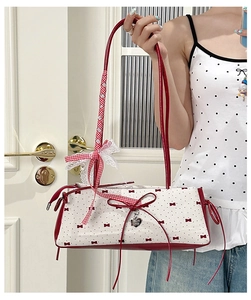 Detailed view of white shoulder bag with red bow prints and silver heart pendant detail