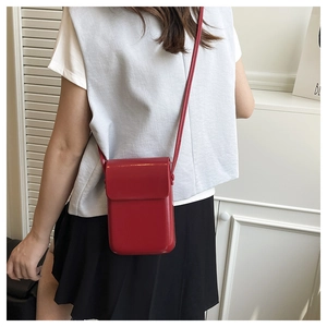 Detalle de mini bolso bandolera rojo en charol brillante usado por una modelo