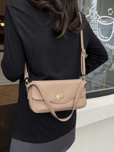 Elegant light brown leather crossbody bag with gold rotating lock in outdoor street setting