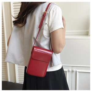 Detail of red patent leather crossbody bag showing the adjustable strap on a model shoulder