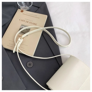 Minimalist beige crossbody phone bag styled on grey blazer with retro book backdrop