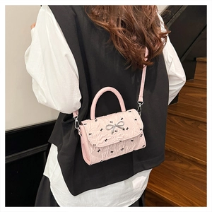 Sac bandoulière plissé rose à motifs de nœuds porté par un mannequin dans un escalier