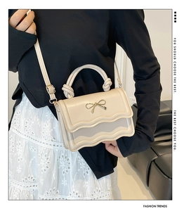 Détail du sac crème avec bordure ondulée et boucle de nœud doré métallique