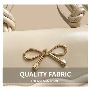 Detail of cream leather shoulder bag featuring golden bow clasp and knotted strap design