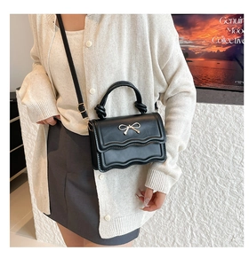 Detail of black crossbody bag featuring a wavy flap and golden butterfly bow hardware