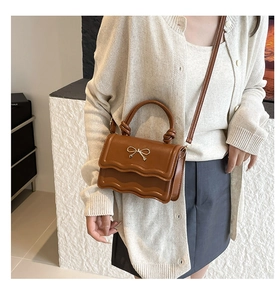 Caramel PU leather bag featuring wave-cut flap, metal bow detail, and knotted handle