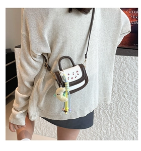 Mini handbag with cherry embroidery, contrast trim, and plush charm on a model's shoulder