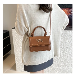 Detail of a brown shoulder bag featuring wavy flap design and metal bow decoration