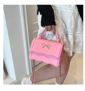 Detailed view of pink wavy edge handbag with gold bow buckle and knotted handle texture