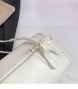 Détail d'un sac à bandoulière en cuir crème avec nœud en satin et poignée en ruban