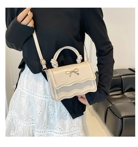 Detailed view of beige bow shoulder bag with wavy flap design on model's outfit