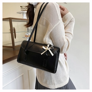 Detail view of black rectangular underarm bag with white satin bow on model's shoulder