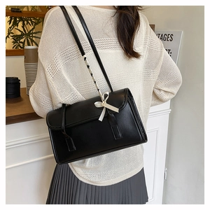 Detail of black leather underarm bag featuring woven strap and cream bow accent on shoulder