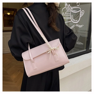Détail du sac baguette rose avec nœud sur la bandoulière devant une boulangerie