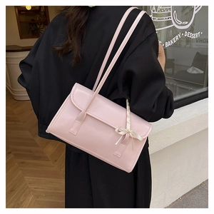 Pink glossy faux leather shoulder bag with bow detail worn by a model in a cafe