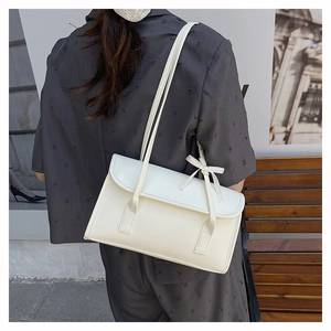 Detail view of cream shoulder bag with ribbon bow and thin straps on a model back