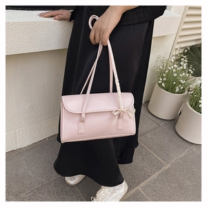 Detail of light pink shoulder bag featuring a white ribbon bow on a smooth leather texture