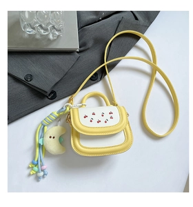 Macro detail of mini yellow cherry clutch with plush moon charm and rainbow tassels