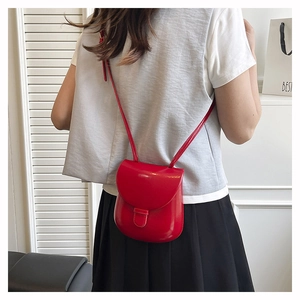 Red faux leather saddle bag worn cross-body by a model in a minimalist modern setting