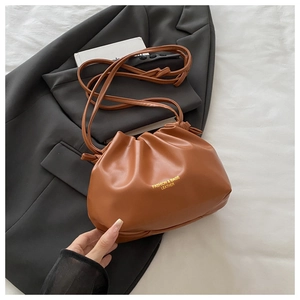Detail of caramel pleated cloud bag in PU leather on a grey blazer and white book