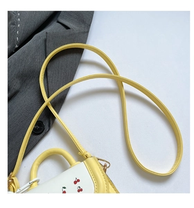 Detail of a mini cherry print handbag featuring yellow and white contrast colors and strap