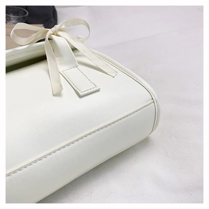 Detail of cream-white leather bag featuring fine stitching and a silk bow decoration
