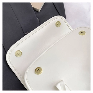 Detail of four gold magnetic snaps on white leather shoulder bag flap with neat stitching