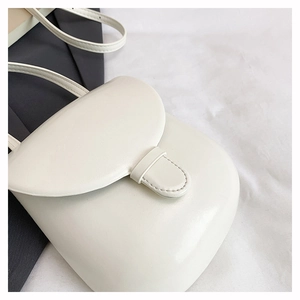 Close-up of cream minimalist crossbody bag featuring rounded flap and vertical buckle strap