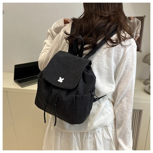 Detail of black grid canvas backpack featuring drawstring closure and unique white buckle
