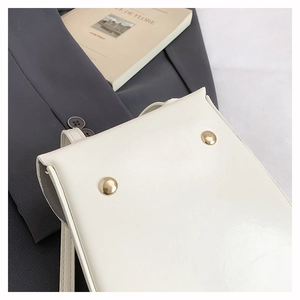 Close-up of minimalist white crossbody phone bag with gold rivets on grey blazer