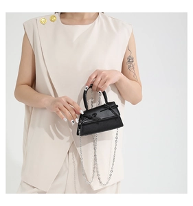 Close-up of a mini black trapezoid handbag with twin bows and silver chain strap