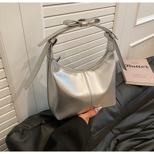 Detail view of metallic silver hobo bag featuring a decorative bow on the shoulder strap