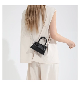 Detailed view of mini black leather bag with double bow design on a white outfit