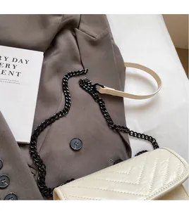 Close-up of beige crossbody bag featuring chevron quilting and bold black chain strap detail
