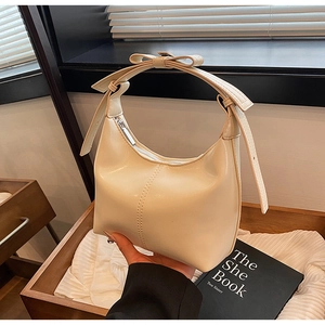 Detail of cream half-moon bag with elegant bow accent and smooth zipper closure