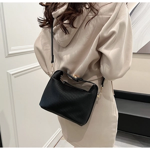 Détail du sac bandoulière noir plissé avec garnitures dorées porté par un mannequin chic