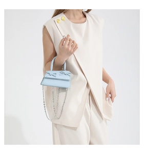Detail of light blue mini handbag featuring elegant twin bows and a silver chain strap