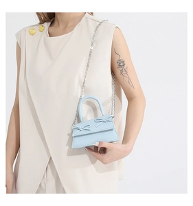 Detail of light blue mini bag with bow accents and silver chain strap on model