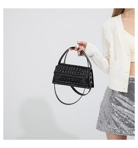 Detailed view of black patent leather handbag featuring geometric quilted texture and handles