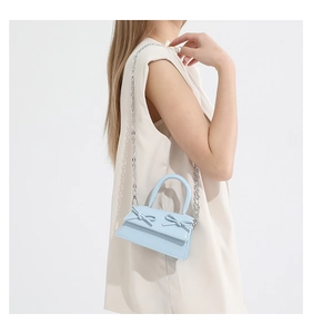 Detail of light blue mini bag featuring decorative bows and a silver chain strap