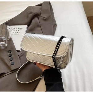 Detail view of metallic silver crossbody bag with V-shaped quilting and black chain strap