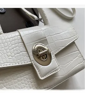 Close-up of golden oval twist lock and white crocodile pattern texture on small handbag