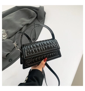 Close-up of black glossy crocodile embossed handbag with metal strap clasp detail