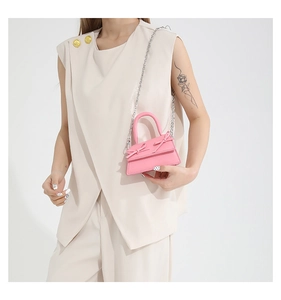 Close-up of pink mini bag with double bows and silver chain strap on beige outfit