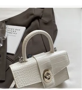 Detail of white crocodile pattern handbag featuring a round silver twist lock closure