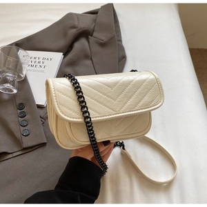 Detail of cream V-quilted flap bag with black chunky metal chain on a grey blazer