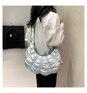 Detail of silver metallic pleated cloud bag with wide shoulder strap and quilted texture
