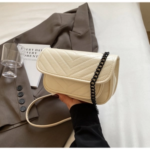 Detail view of cream quilted leather crossbody bag with V-shaped stitching and chain strap